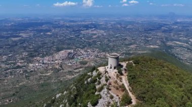 Issız bir kule bir tepenin üzerinde duruyor, yemyeşil vadiyi, antika kasabayı ve berrak mavi gökyüzünün altında yuvarlanan dağları panoramik bir şekilde gösteriyor..