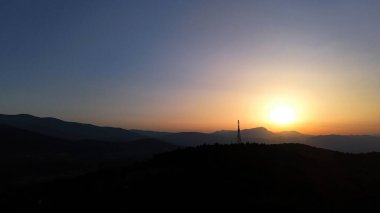 Güneş yavaşça yükseliyor, dağ manzarası üzerine sıcak bir parıltı saçıyor, doğa uyanıkken, canlı gökyüzüne karşı siluetleri aydınlatıyor..