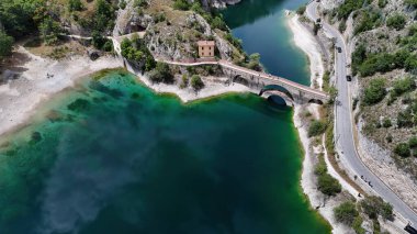 Bu büyüleyici manzara, arka planda manzaralı tepeleri olan ve turkuaz suların üzerinde zarif bir şekilde uzanan antik bir köprüyü gözler önüne seriyor..