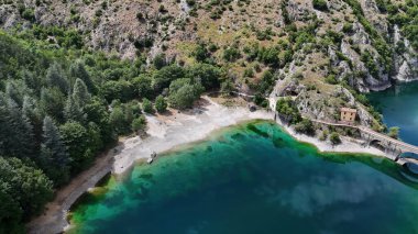 Gözlerden uzak bir kıyı şeridinin nefes kesen manzarası çevredeki kayalıkları ve parlak bir yaz gökyüzünün altındaki canlı yeşillikleri yansıtan kristal berraklığında suları ortaya çıkarıyor..