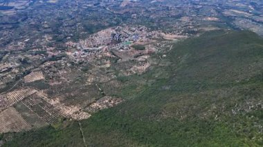 Hava perspektifi, yemyeşil bir vadide yuva yapmış küçük bir kasaba üzerinde yavaşça geziniyor, insan yerleşimi ve doğanın barışçıl birlikteliğini gösteriyor.