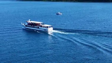 Feribot, güneşli bir yaz gününde turistleri taşırken ardında bir uyanış bırakarak bir gölü geçiyor.