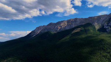 Bulutlar yavaşça yeşil ormanlarla kaplı bir dağ sırasının üzerinden geçiyor.
