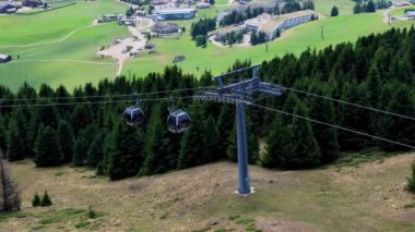 Teleferik turistleri dağlardaki bir tatil köyünün yakınındaki yeşil bir ormandan taşıyor.
