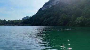 Güneş, bir dağ gölünün sularına yansıyor. Turistler manzaranın keyfini çıkarıyor.
