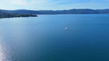 Yalnız yelkenli, Bracciano gölünün sakin sularında süzülüyor. Arka planda pitoresk bir kasaba ve Rocca dei Orsini kalesi var.