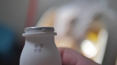 Bir insan taze tarih ve saatini gösteren narin bir süt şişesi tutar. Arka plan, sıcak ve davetkar renklerle dolu sıradan bir mutfak ortamını işaret ediyor..