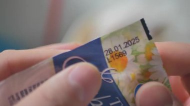 Bir kişi, belirli bir son kullanma tarihini gösterirken çiçekli tasarımlar içeren canlı bir banknotu inceler. Atmosfer tesadüfi ve tuhaf, yakından incelemeye davet ediyor..