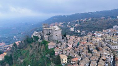 Kayalık bir tepenin tepesine tünemiş görkemli bir kale, yemyeşil yemyeşil bir yere kurulmuş tuhaf bir köyün panoramik manzarasına hükmediyor. Mimari, taş duvarlar ve taretlerle yüzyılların tarihini yansıtıyor.