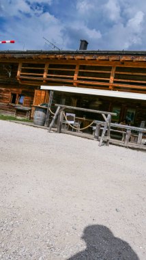 Dağlarda yuva yapmış büyüleyici bir pansiyon ahşap mimariyi mavi gökyüzünün zeminine karşı sergiliyor. Güneş ışığı, dışarıdaki oturma yerlerini karşılayan çakıllı bir patikayı aydınlatıyor..