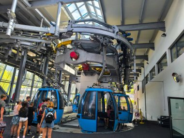 Hevesli yolcularla dolu canlı bir teleferik istasyonu manzaralı bir dağ yolculuğuna çıkmak için sıralarını bekliyor. Cam duvarlar, heyecan arttıkça çevredeki manzarayı görmenizi sağlar..