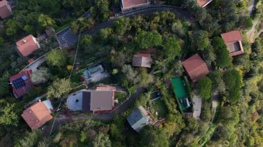 Gökyüzü manzarası tepelerde yuva yapmış, evleri, virajlı yolları ve canlı yeşillikleri gösteriyor. Huzurlu atmosfer huzuru ve cazibeyi çağrıştırıyor..