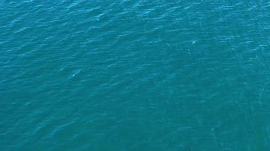 Camsı turkuaz sular, parlak mavi bir gökyüzünün altında durmaksızın uzanıyor. Düşünme ve rahatlama için mükemmel sakin bir atmosfer yaratıyor. Yumuşak dalgalar yüzeyde dans eder, güneş ışığını yansıtır..