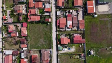 Hava manzarası, yemyeşil bölgelerle çevrili kırmızı çatıları olan evlerin büyüleyici düzenini yakalıyor. Güneş parlıyor, mahallenin organize düzenini vurguluyor..