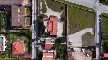 Hava perspektifi, kırmızı çatıları ve bahçeleri olan büyüleyici evleri olan canlı bir mahalle yakalıyor. Yakınlarda boş bir arazi var, dolambaçlı yollar ve açık bir gökyüzünün altında yeşilliklerle çevrili..