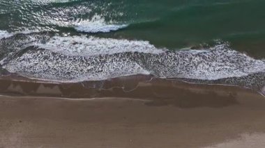 Yumuşak dalgalar kumlu kıyı şeridini okşayarak barışçıl bir atmosfer yaratır. Güneş suların yüzeyinde parıldıyor. Huzurlu bir sahil ortamında rahatlamaya ve yansımaya davetiye çıkarıyor..