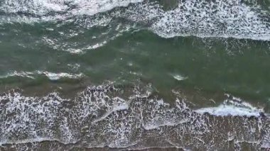 Yumuşak dalgalar kumlu sahile doğru ritmik bir şekilde akarken dalgalar güneşin altında parlıyor. Martılar başımızın üstünde süzülerek huzurlu bir öğleden sonranın sakin sahil atmosferini güçlendiriyor..