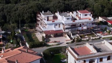 Yoğun bir yeşillik zemininin ortasında, modern bir konut inşaatı sürüyor. İnşaat iskelesi, işçilerin toplumsal cazibesini özenle artırmasıyla yapıyı kaplıyor..