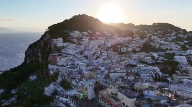 Şafak vakti Capri 'nin büyüleyici manzarası, yamaçlardan aşağı dökülen beyazlatılmış binalar, sakin bir deniz ve manzarayı aydınlatan altın güneş ışığı ile çevrili..