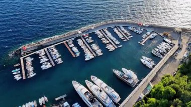 Yatlar ve tekneler hareketli bir marinaya demirlemiş, parlak mavi bir deniz ve sudan yansıyan güneş ışığı var. Canlı atmosfer, deniz yaşamının özünü en iyi şekilde yakalar..