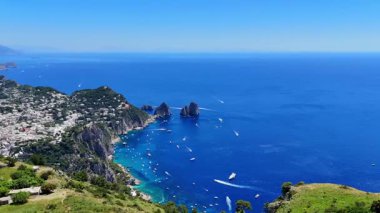 Vibrant blue waters sparkle under the sun as sailboats glide across the coastline of Capri. A picturesque village rests on lush green hills, offering a stunning backdrop to this serene paradise.