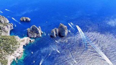 From above, the sunlit shores of Capri reveal a tapestry of azure waters and rocky formations, as boats gracefully weave through the tranquil sea on a warm summer afternoon