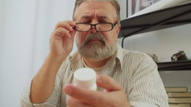Gözlüklü, sakallı, yakışıklı bir adamın portresi tüp hap kutusunda reçeteli ilaç metni okuyor, uyuşturucu belirtileri ve zıtlıkları hakkında bilgi ediniyor..