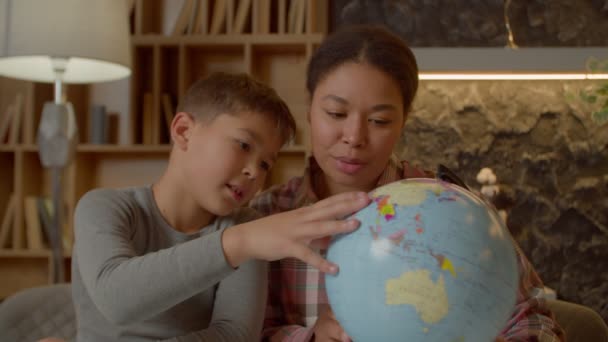 愛らしい多人種の小学生の息子の肖像と世界地図で世界を勉強魅力的なアフリカ系アメリカ人の母親を世話し 国内部屋で地理の宿題をする — ストック動画