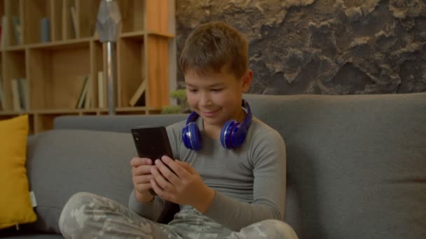 Θετική Αξιολάτρευτο Πολυφυλετικό Στοιχειώδες Αγόρι Ηλικίας Κάθεται Σταυροπόδι Στον Καναπέ — Αρχείο Βίντεο