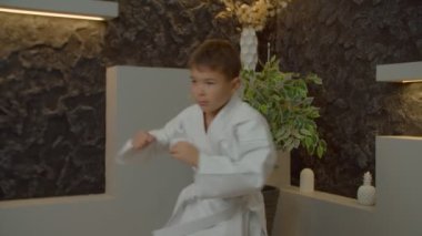 Beyaz kimonolu çok kültürlü karateci çocuk içeride egzersiz yaparken karate antrenmanı yapıyor, gösteri yapıyor ve yumruk tekniğini geliştiriyor..