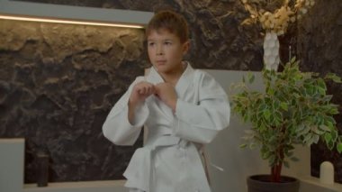 Kimono giyen, karate eğitimi alan, iç mekanda spor yaparken dirsek bloğu tekniklerini geliştiren ve uygulayan kararlı, çok ırklı karateci çocuk..