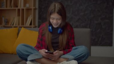 Sevimli, tapılası İspanyol ergen kız, kanepede bağdaş kurarak oturuyor, akıllı telefondan iletişim kuruyor, mesajlaşıyor ve sosyal medya içeriğini araştırıyor..