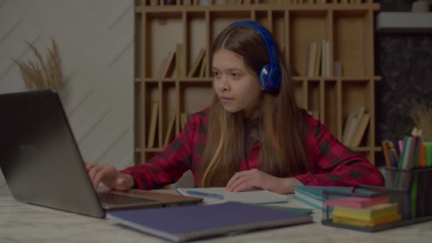 值得称道的是 西班牙裔少女集中在家里的无线耳机里 使用笔记本电脑 学习在线课程 并在练习本上写作业 — 图库视频影像