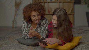 Mutlu, çok kültürlü genç kız ve neşeli siyah anne yerde dinleniyor, konuşuyor ve sosyal medya içeriğini internette araştırıyor..