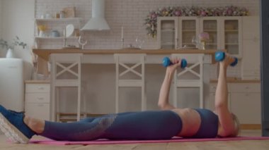 Kararlı motive edici çekici spor olgun kadın ağırlık çalışması yapıyor, dambıl zemini presi yapıyor, göğüs, omuzlar, deltoidler ve trisepsler gücünü arttırıyor..