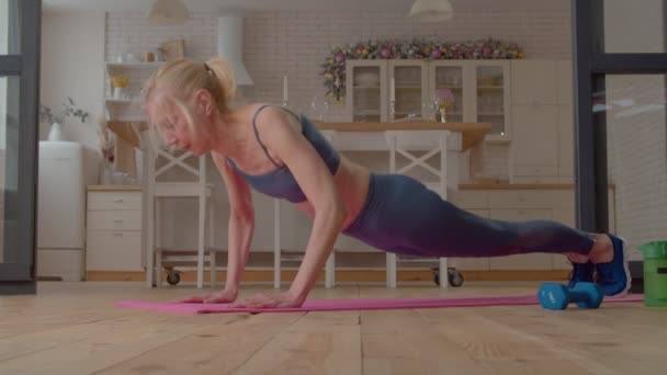 ヨガの板の位置に立って積極的にフィットネス成熟した女性を決定しました 背骨を強化 Rhomboids そして 自宅で作業しながら 腹部の筋肉 — ストック動画