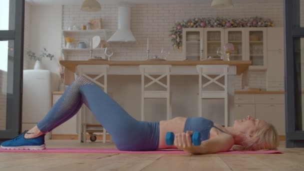 在室内锻炼中 穿着运动服躺在瑜伽垫上 练习哑铃式胸肌飞舞 增加肩膀和核心力量 以此来确定积极健康迷人的成熟女性 — 图库视频影像