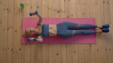 Spor kıyafetleriyle uyumlu, etkin ve olgun bir kadının spor salonunda ağırlık antrenmanı yaparken kafatası ezme egzersizi, tonlama ve artan trisepslerin genel görünüşü..