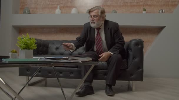 魅力的なひげそり成人男性幹部がソファに座って ビジネス上の問題について考え オフィスで働く中で会社の戦略について決定を下す — ストック動画