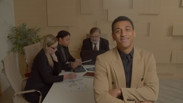 一位成功 英俊的非裔美国男性企业主管的画像 他双臂交叉地站在一边 对背景各异的多种族同事友好地微笑着 — 图库视频影像