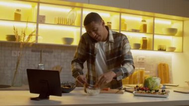 Portrait of attractive multitasking busy with smartphone African American man preparing tasty snack with fresh salmon and cheese, expressing positivity and happiness in domestic kitchen.