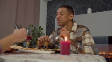 Romantic cheerful African American man and beautiful happy black female talking and bonding, tasting delicious food, enjoying beautiful moments together while having dinner at home.