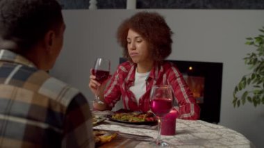 Positive loving black man surprising excited attractive African American woman, giving passports with travel tickets for romantic summer trip while couple celebrating event at festive table.