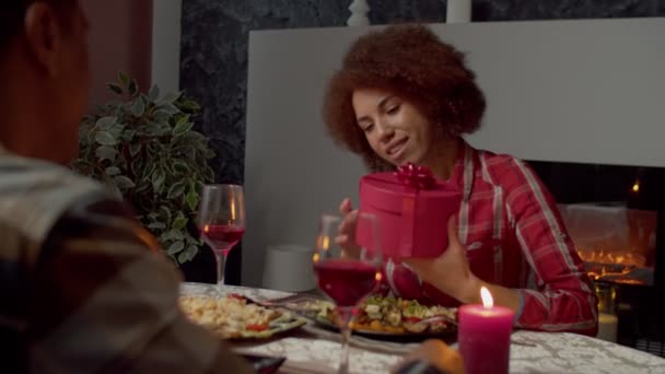 愛するアフリカ系アメリカ人男性がバレンタインデーにプレゼントを推測しようとしながら カップルはお祝いのテーブルでリラックスしながら 魅力的な興奮した黒の女性の握手ギフトボックスの肖像画 — ストック動画