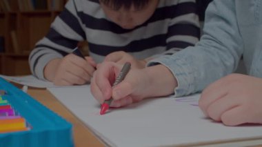 Close-up of children hands with colorful crayon and felt tip pen drawing picture on paper sheet, developing artistic skills and creativity while kids spending leisure and having fun at home.