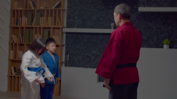 动情的小学亚洲跆拳道学生与弓箭手专业的资深男性武术大师打招呼 表现出对体育训练的尊重和准备 — 图库视频影像