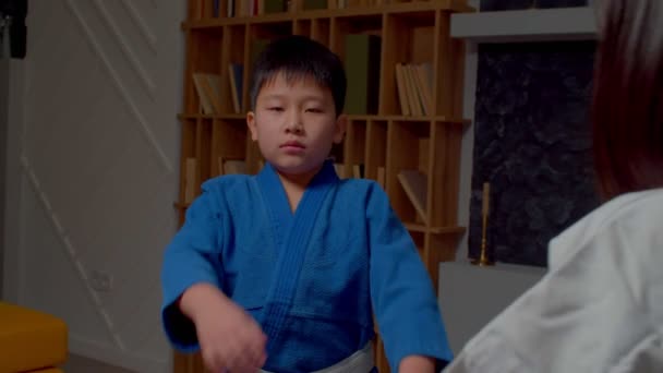穿着制服站在对抗对手的战斗姿态上 准备参加比赛 在室内表现出自信和决心的可爱的小学武术亚洲男孩的画像 — 图库视频影像