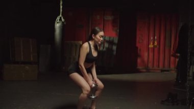 Aktif kıyafetli, çekici ve çekici bir kadın halterci, dambıl egzersizi yapıyor, spor salonunda spor yaparken alt vücut ve vücut kaslarını güçlendiriyor..