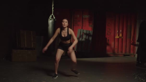 决心积极吸引人的运动健美亚洲女人进行有氧运动 以取得平衡 敏捷和机动性 进行滑雪者跳跃运动 在黑暗的车库健身房锻炼下半身力量 — 图库视频影像