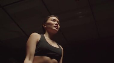 Kararlı motivasyonlu sporun portresi çekici Asyalı bir kadının ağırlık çalışmasına uyuyor, koyu renk spor salonunda egzersiz yaparken halterli biseps egzersizleri yapıyor. Düşük açı görünümü.